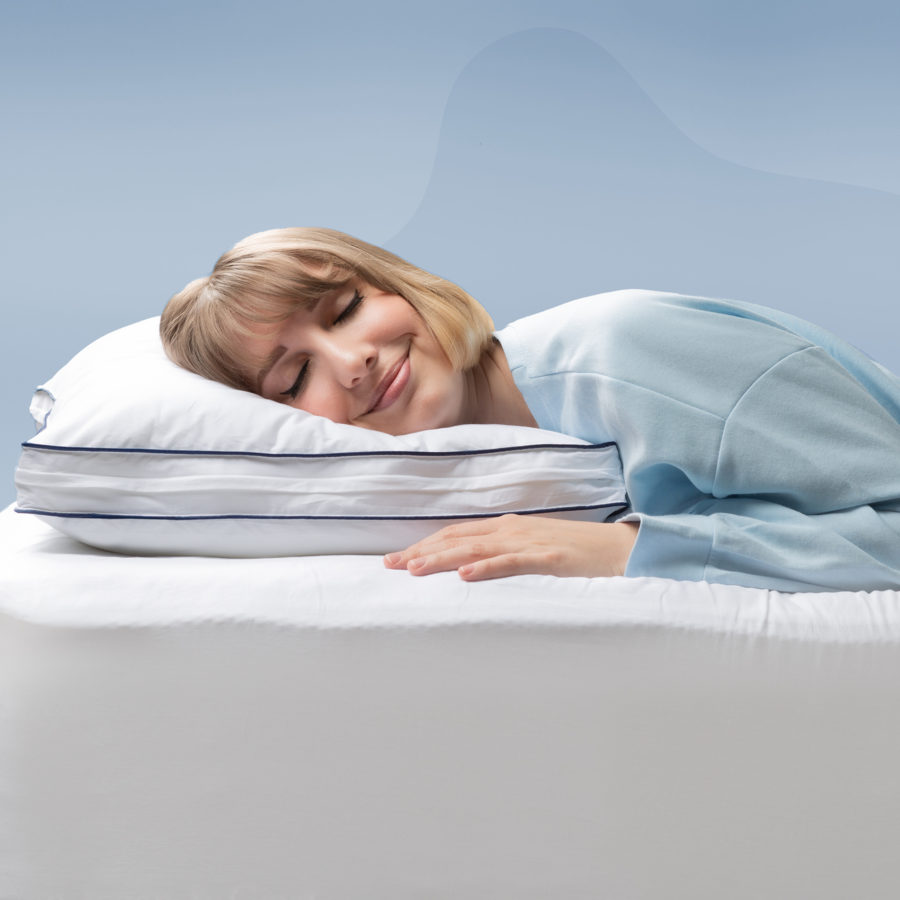 A woman smiles as she rests her head on a Juno Adjustable Memory Foam Pillow.
