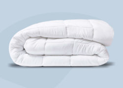 Une couette alternative en duvet toutes saisons est soigneusement pliée sur un fond bleu clair.