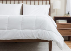 La couette alternative en duvet Juno est soigneusement étalée sur un matelas Juno qui repose sur un ensemble de lit en bois.