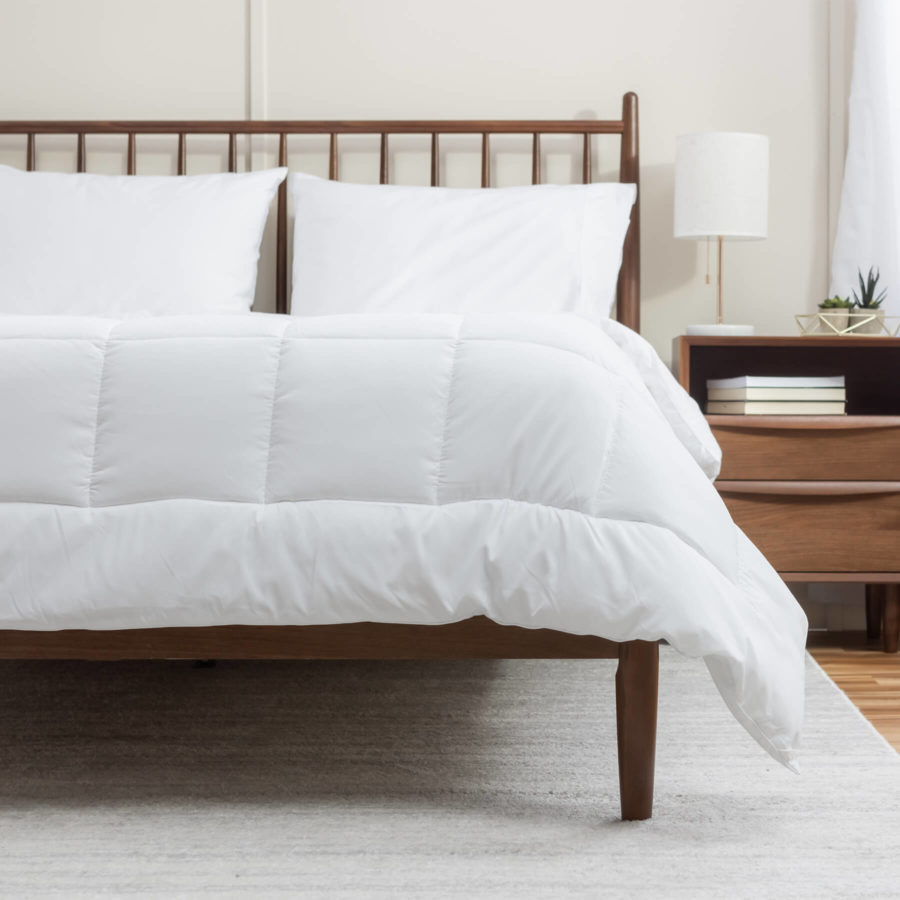 La couette alternative en duvet Juno est soigneusement étalée sur un matelas Juno qui repose sur un ensemble de lit en bois.