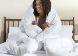 A woman wraps the Juno down alternative duvet snugly around her body while sitting on a Juno mattress.