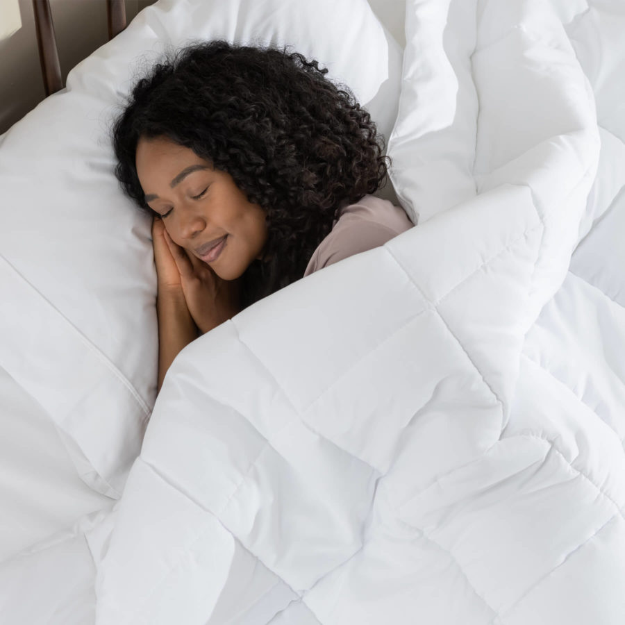 Une femme dort sur son matelas Juno sous une couette alternative en duvet Juno blanc brillant.