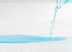 Un liquide bleu est versé sur le protège-matelas Juno pour montrer ses qualités protectrices et absorbantes.