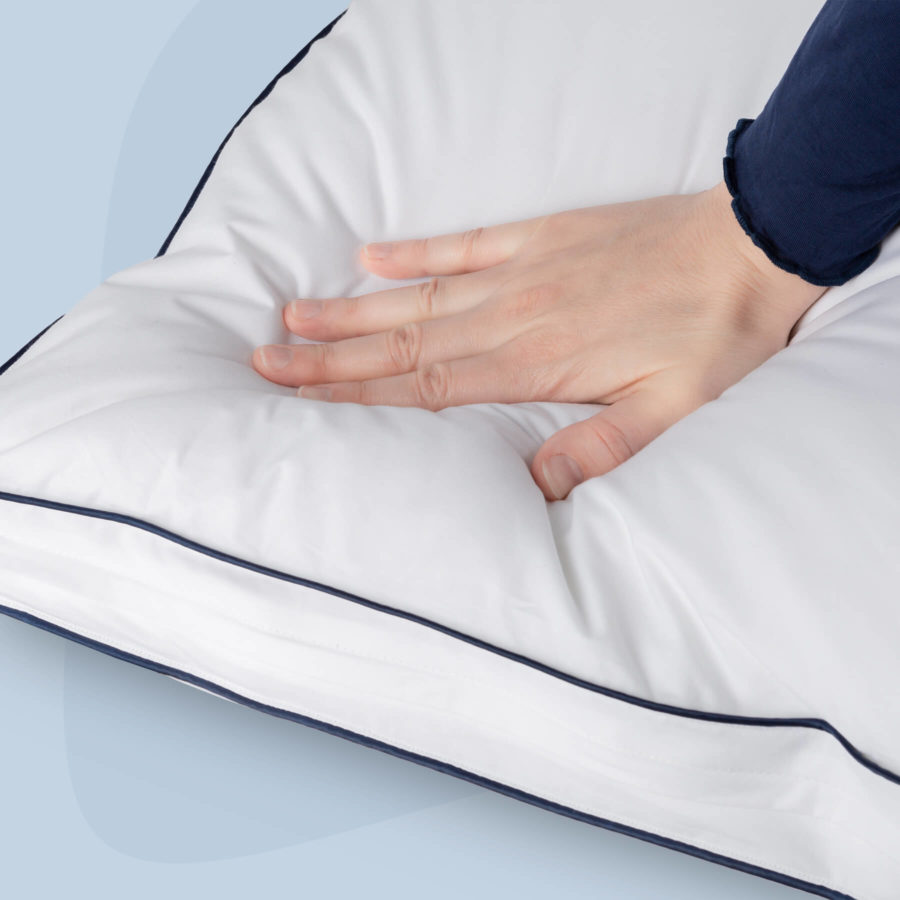 A hand presses down on the Juno Adjustable Memory Foam Pillow to display pressure relief.