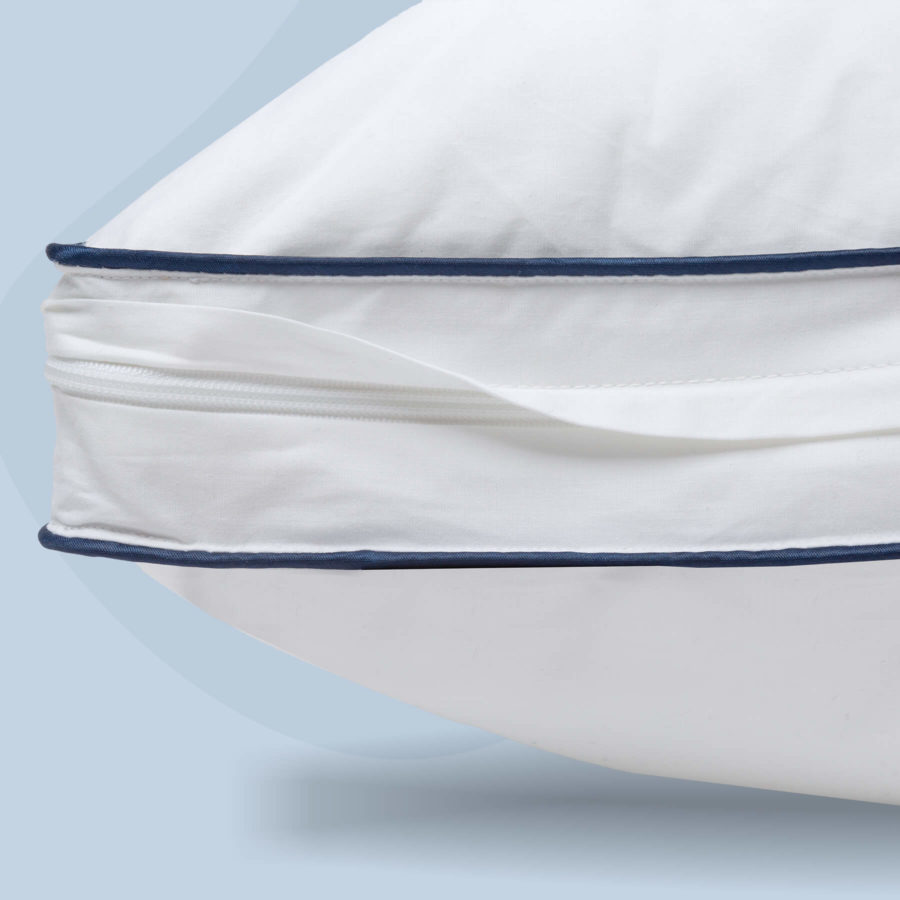 A close up of the zipper on the Juno Adjustable Memory Foam Pillow. The zipper is surrounded by two dark blue seams and the pillow is set against a light blue background.
