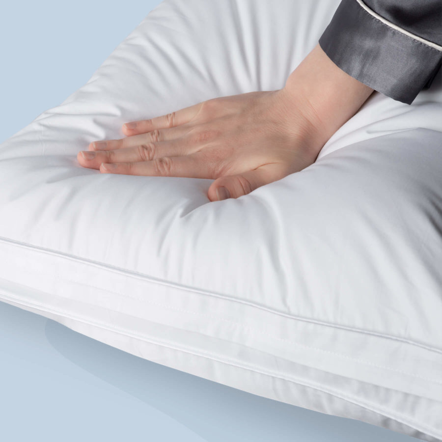 A hand presses down on the Juno Microfiber pillow displaying its pressure relief capabilities.