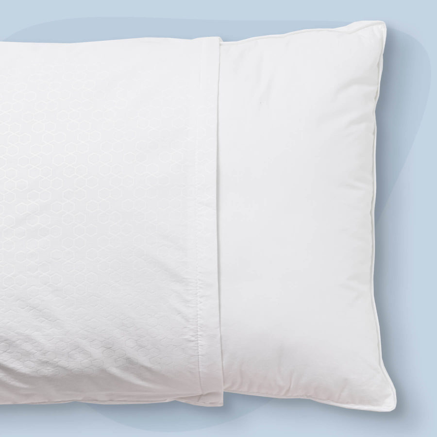 A Juno Pillow Protector is pulled slightly off a pillow to show the snug fit and difference in material.