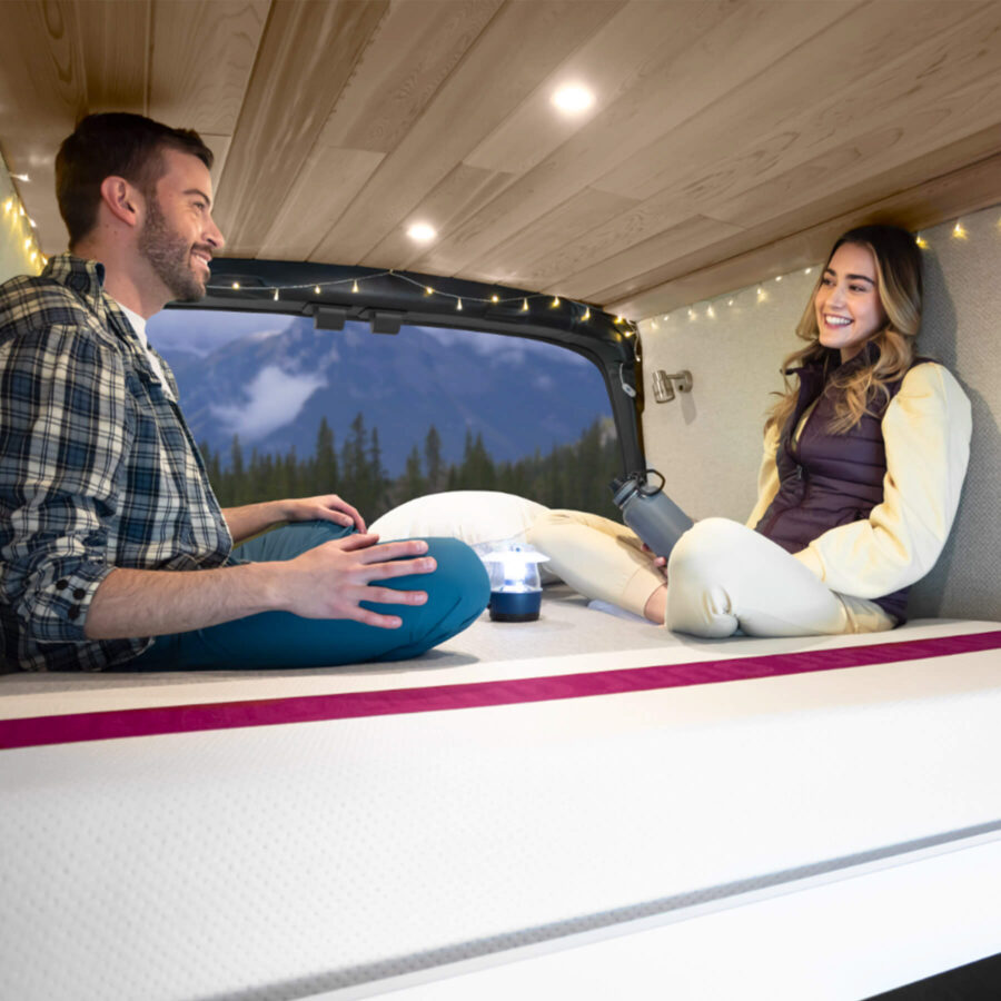 Man and woman similing and sitting on Juno mattress in an RV