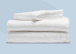 Un drap de dessus, un drap-housse et une taie d'oreiller sont soigneusement pliés sur un fond bleu clair.