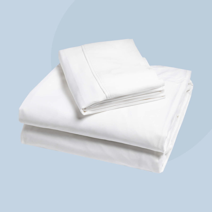An angled view of a Juno top sheet, fitted sheet, and pillow cover sit neatly folded against a light blue background.
