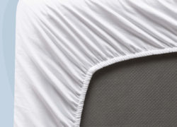 A bottom-corner view of a Juno sateen sheet set, showcasing the stretchy elastic that snugly fits the sheets to your mattress.