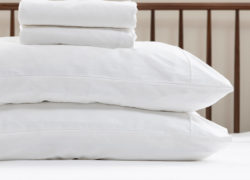 Two pillows in Juno pillow covers sit on a Juno mattress with a top sheet and fitted sheet neatly folded on top.