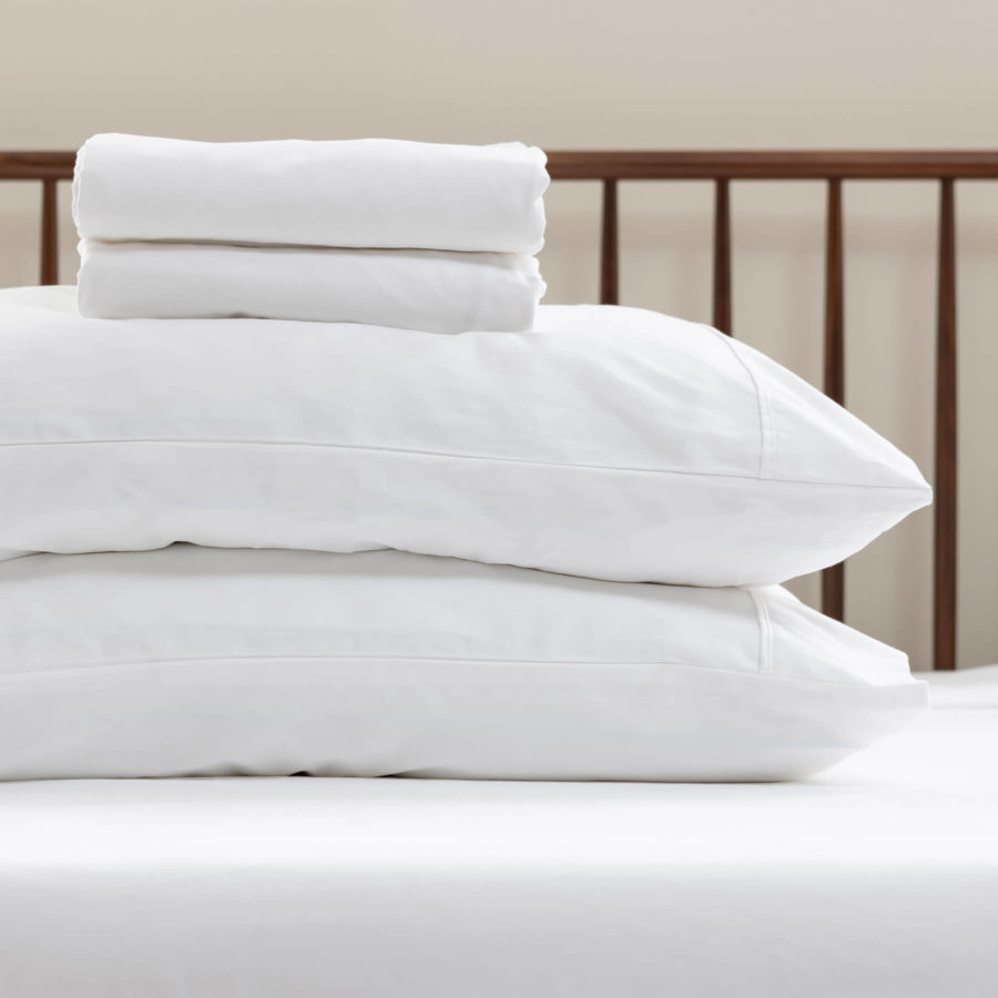 Two pillows in Juno pillow covers sit on a Juno mattress with a top sheet and fitted sheet neatly folded on top.