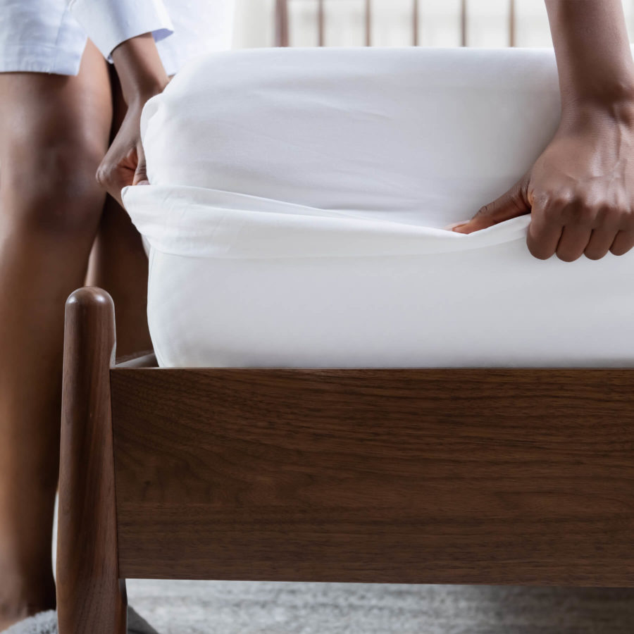 A woman stretches a Juno sateen sheet over her mattress.