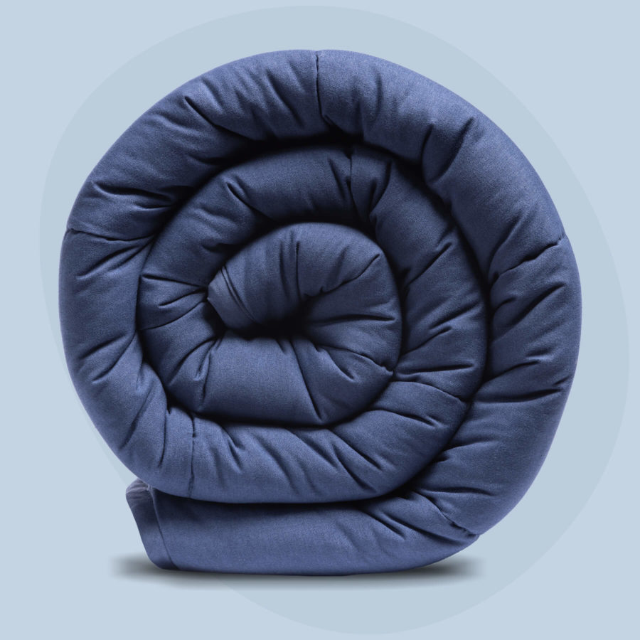 A Juno Weighted Blanket sits against a light blue background, neatly rolled up into a tight spiral.