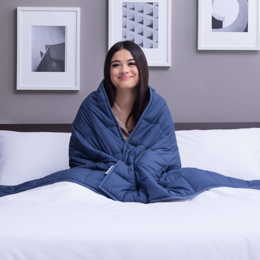 Une femme assise sur un matelas Juno avec la couverture lestée Juno serrée autour de ses épaules.