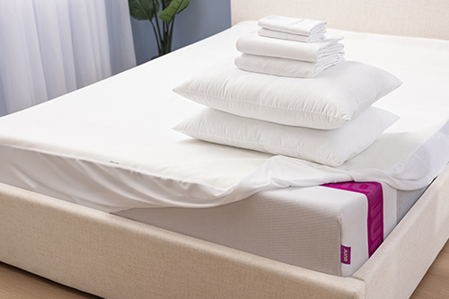 A series of bedding items and pillows lay on top of a Juno mattress for the Build a Bundle promotion. 
