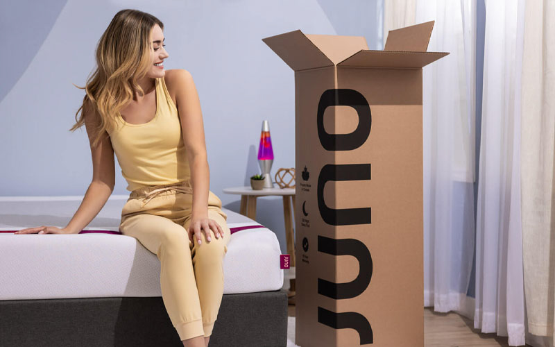 Woman sitting on Juno mattress, looking at the delivery box