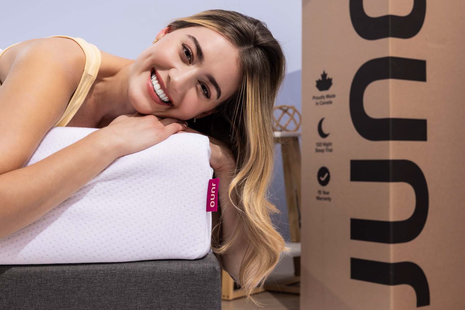 Femme souriante sur un matelas Juno avec boîte d'expédition à côté d'elle