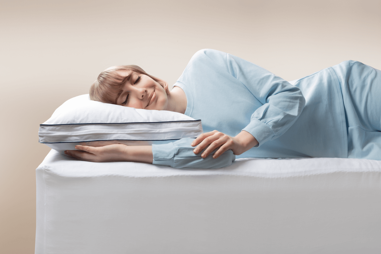 A woman smiles as she lays down and rests her head on an adjustable memory foam pillow.
