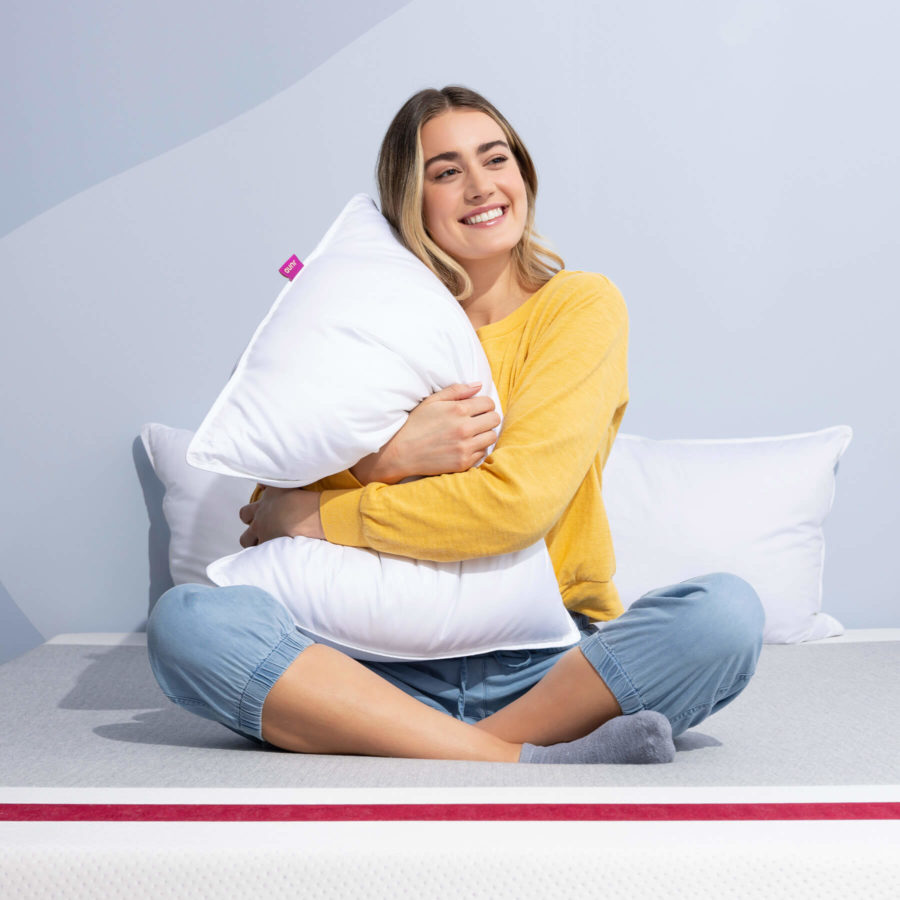 Woman sitting cross-legged and hugging a Juno Down Alternative Pillow